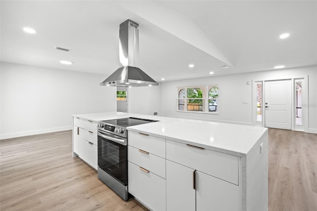 kitchen with stainless steel range with electric stovetop, light stone counters, island range hood, and light hardwood / wood-style floors