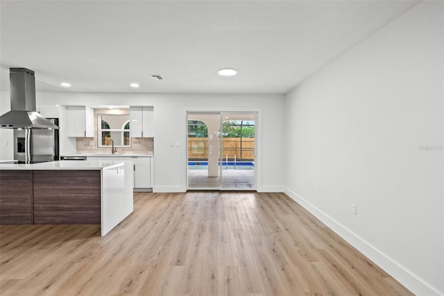 kitchen featuring island range hood, decorative backsplash, white cabinets, and light wood-type flooring