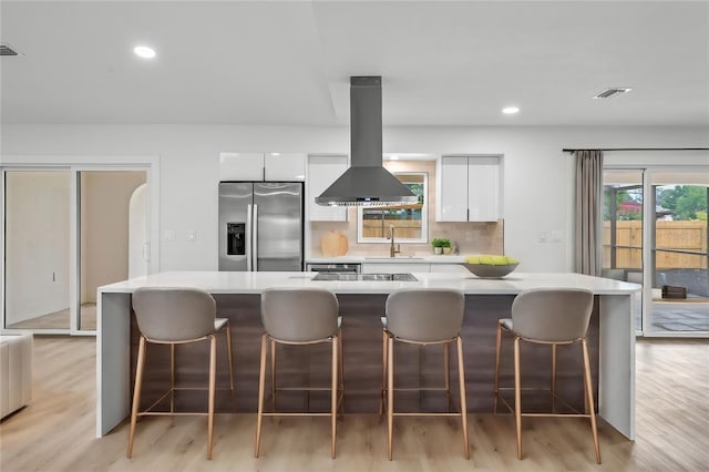 kitchen featuring a kitchen island, island exhaust hood, white cabinets, and stainless steel refrigerator with ice dispenser