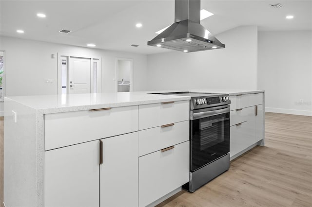 kitchen featuring stainless steel electric range, light hardwood / wood-style floors, light stone countertops, island exhaust hood, and white cabinetry