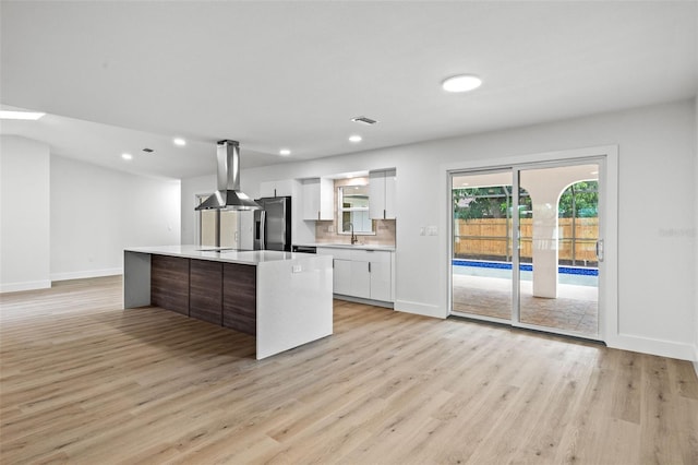 kitchen featuring white cabinets, a center island, light hardwood / wood-style floors, island range hood, and stainless steel refrigerator with ice dispenser