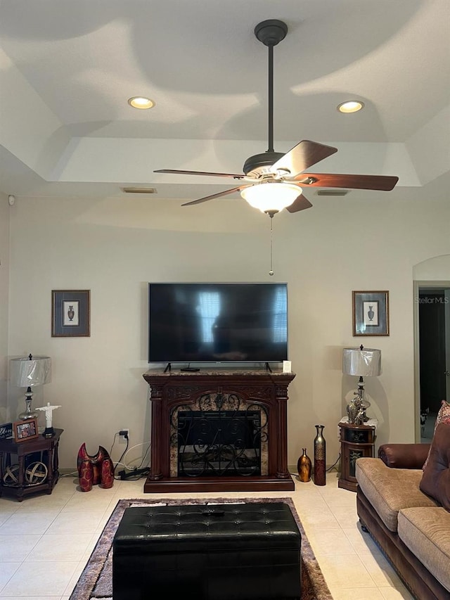 living room featuring ceiling fan, light tile floors, and a tray ceiling