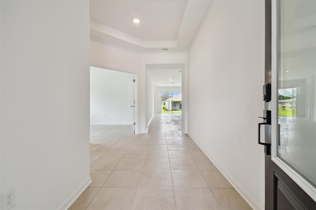 hall featuring light tile patterned flooring and a tray ceiling