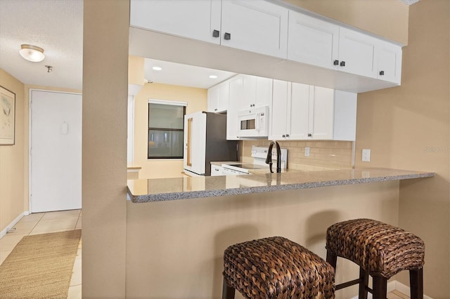 kitchen featuring white appliances, tasteful backsplash, kitchen peninsula, and light stone counters