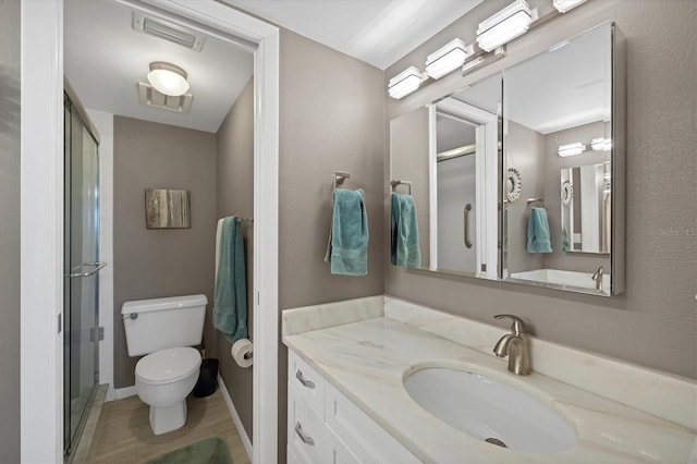 bathroom featuring a shower with shower door, toilet, and vanity