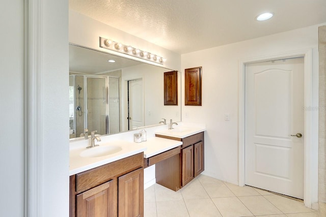 bathroom with a shower with door, vanity with extensive cabinet space, tile flooring, a textured ceiling, and double sink