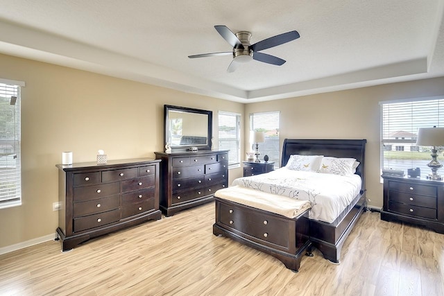 bedroom featuring a raised ceiling, light hardwood / wood-style floors, ceiling fan, and multiple windows