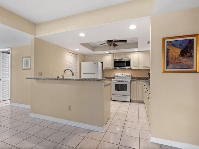 kitchen with cream cabinets, white appliances, light tile flooring, a tray ceiling, and dark stone counters