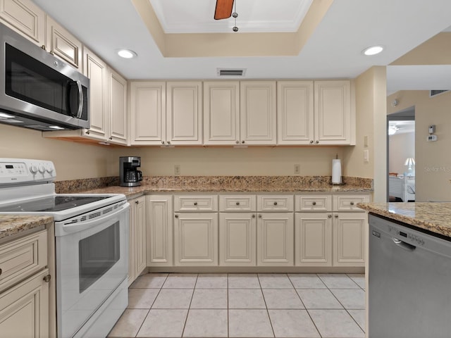 kitchen with cream cabinets, light stone countertops, ceiling fan, stainless steel appliances, and a tray ceiling