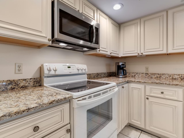 kitchen featuring cream cabinetry, electric range, light tile floors, and light stone countertops