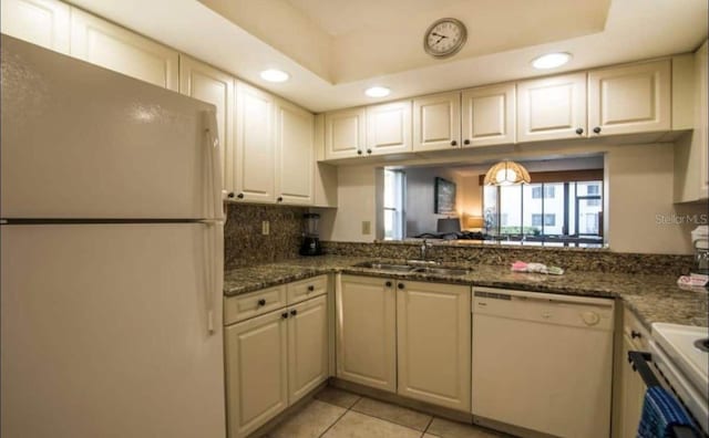 kitchen with light tile floors, sink, white appliances, a tray ceiling, and dark stone counters