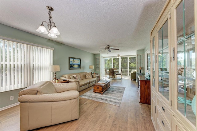 living room featuring ceiling fan with notable chandelier, light hardwood / wood-style flooring, and a textured ceiling