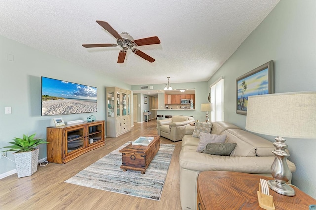 living room featuring ceiling fan with notable chandelier, light wood-type flooring, and a textured ceiling