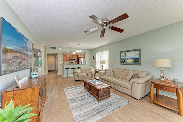 living room with light hardwood / wood-style floors, ceiling fan with notable chandelier, and a textured ceiling