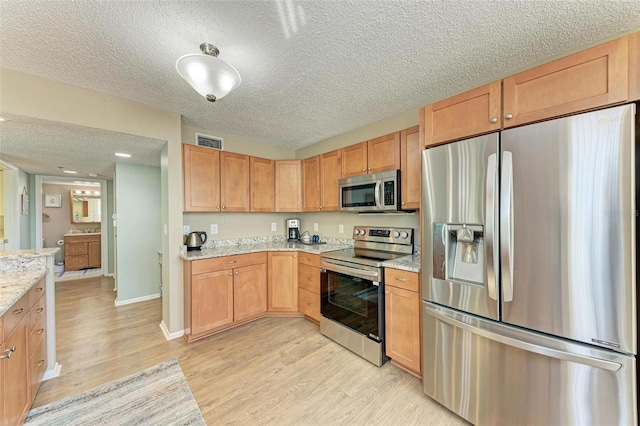 kitchen with a textured ceiling, light hardwood / wood-style floors, appliances with stainless steel finishes, and light stone counters