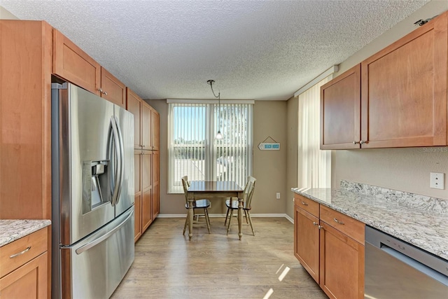 kitchen featuring decorative light fixtures, stainless steel appliances, light hardwood / wood-style floors, a textured ceiling, and light stone counters