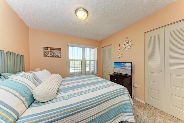 bedroom featuring light carpet, two closets, and a textured ceiling