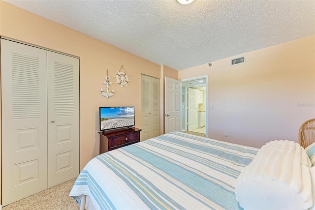 bedroom featuring light colored carpet, a textured ceiling, and two closets