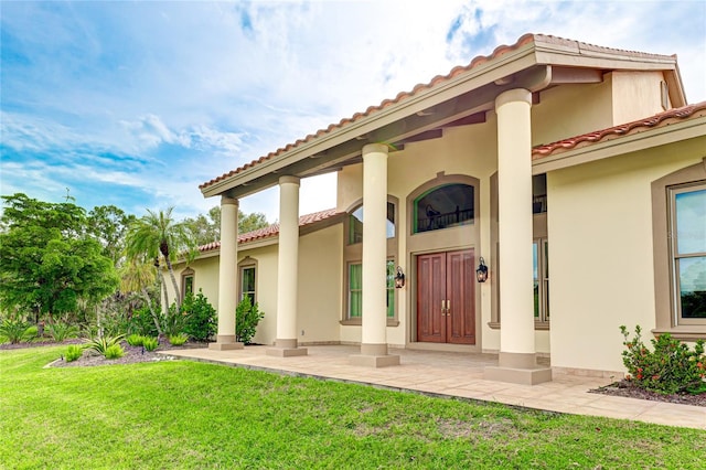 doorway to property featuring a yard, a tiled roof, and stucco siding