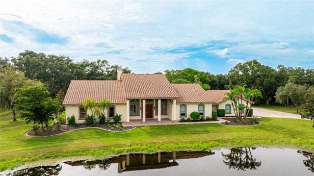 view of front of property featuring a tile roof, a chimney, a water view, a front lawn, and stucco siding