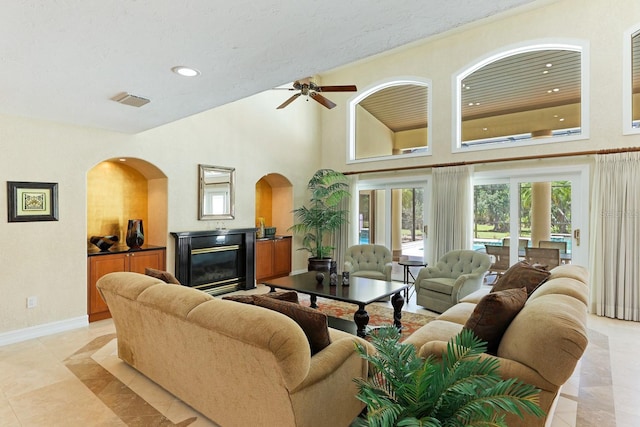 living room with visible vents, baseboards, a glass covered fireplace, a towering ceiling, and recessed lighting