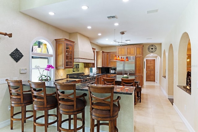 kitchen with premium range hood, high quality appliances, brown cabinetry, and backsplash