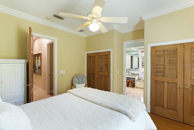 bedroom featuring ceiling fan, visible vents, ornamental molding, light wood finished floors, and two closets