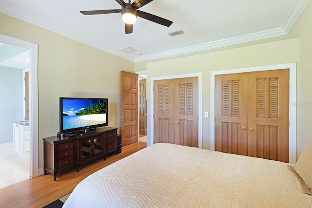 bedroom featuring crown molding, two closets, visible vents, ensuite bath, and wood finished floors