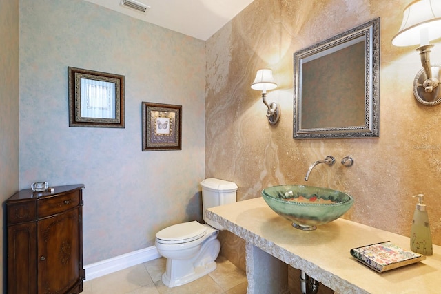 half bath with tile patterned flooring, toilet, a sink, visible vents, and baseboards