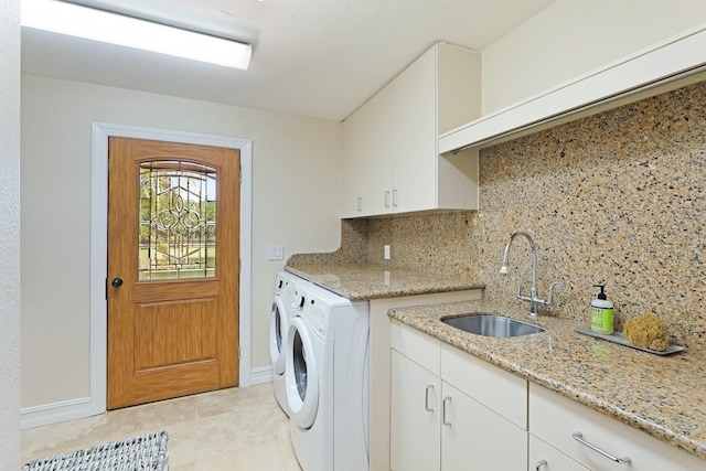 clothes washing area featuring cabinet space, baseboards, washer and dryer, and a sink