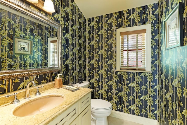 bathroom featuring baseboards, vanity, toilet, and wallpapered walls