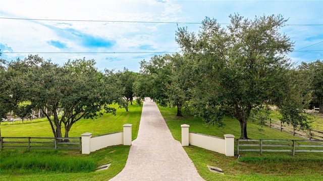 view of community featuring a fenced front yard, decorative driveway, a lawn, and a rural view