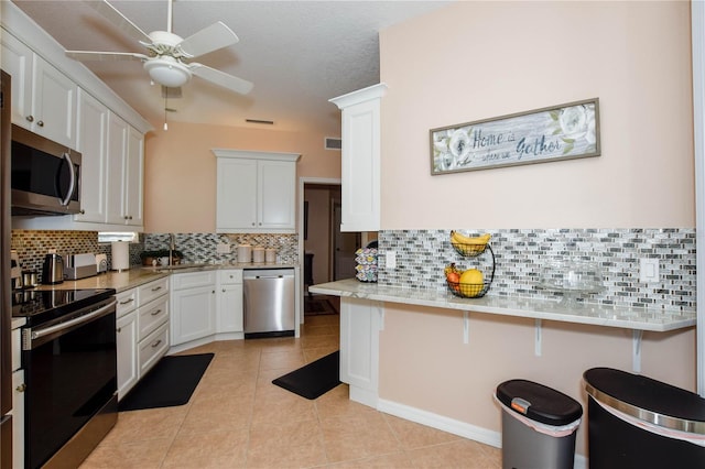 kitchen featuring backsplash, ceiling fan, stainless steel appliances, white cabinets, and a kitchen breakfast bar