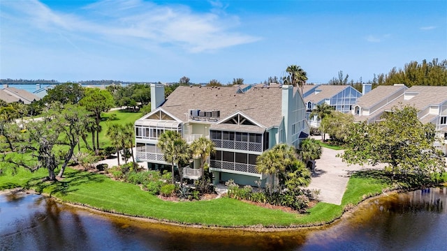 rear view of property featuring a water view, a yard, and a sunroom