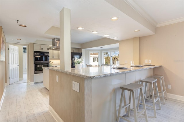 kitchen with light stone countertops, multiple ovens, light wood-type flooring, and kitchen peninsula