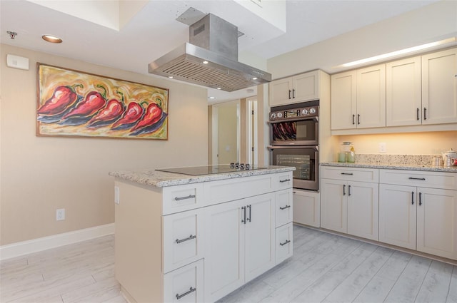 kitchen with a center island, light stone counters, island range hood, black electric cooktop, and stainless steel double oven