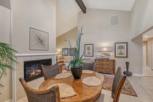 dining area with high vaulted ceiling, a tiled fireplace, beamed ceiling, and light tile floors