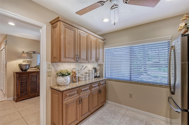 kitchen featuring ceiling fan, light stone countertops, light tile floors, and stainless steel refrigerator