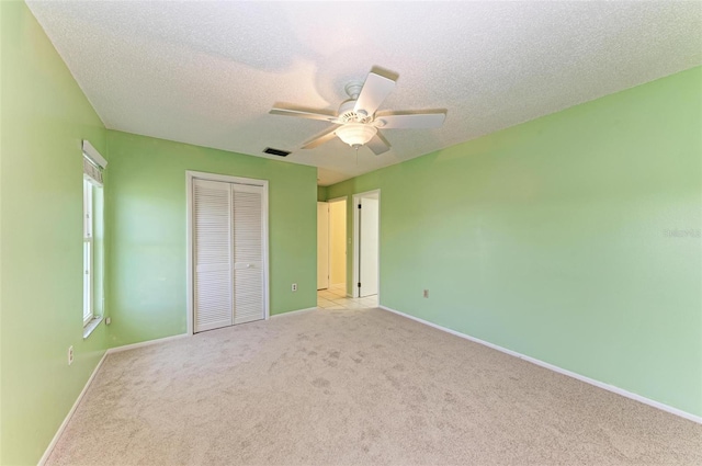 unfurnished bedroom featuring light colored carpet, a textured ceiling, ceiling fan, and a closet