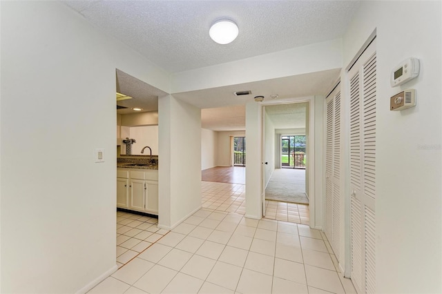 hallway with a textured ceiling, sink, and light tile floors