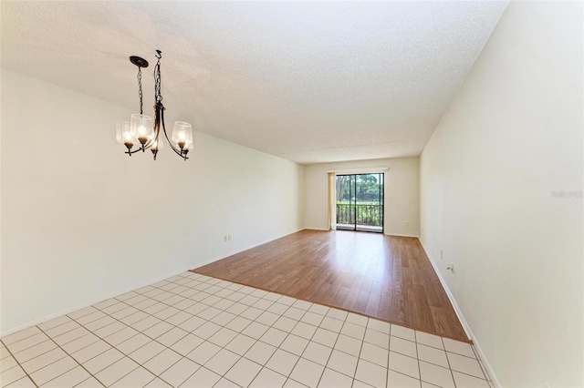 spare room with light hardwood / wood-style flooring, a chandelier, and a textured ceiling