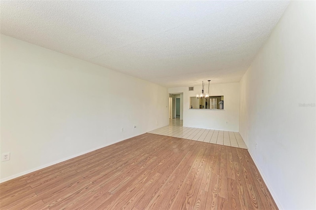 unfurnished living room featuring a textured ceiling, light hardwood / wood-style floors, and an inviting chandelier