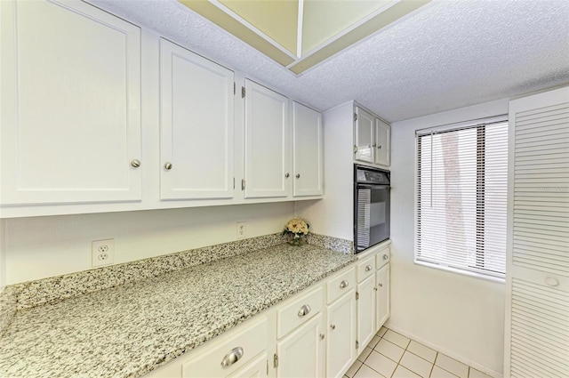 kitchen with oven, light tile flooring, white cabinets, and light stone countertops