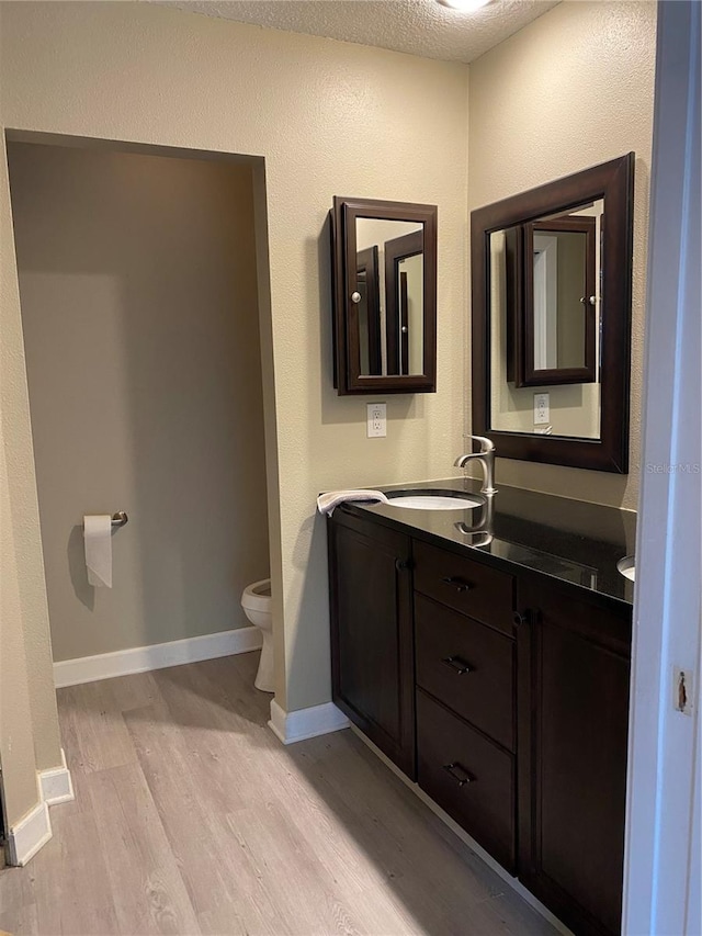 bathroom featuring wood-type flooring, vanity, toilet, and a textured ceiling