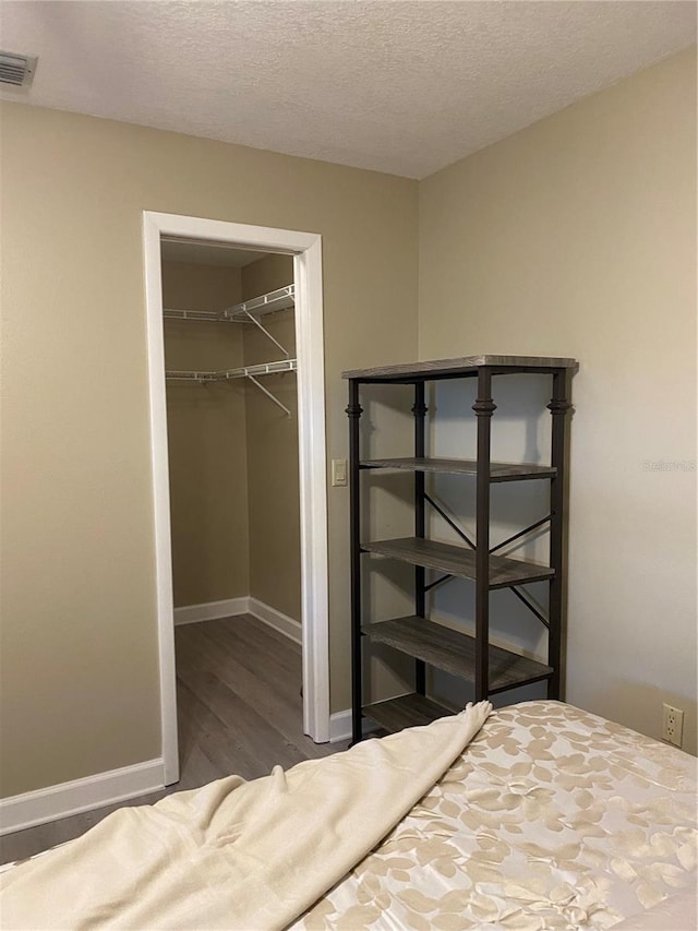 unfurnished bedroom featuring a spacious closet, a closet, dark wood-type flooring, and a textured ceiling