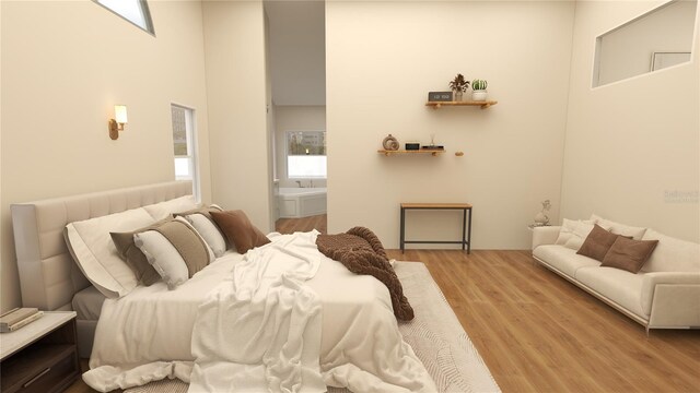 bedroom with a towering ceiling, connected bathroom, and light wood-type flooring