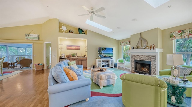 living room with plenty of natural light, light hardwood / wood-style flooring, lofted ceiling with skylight, and a stone fireplace