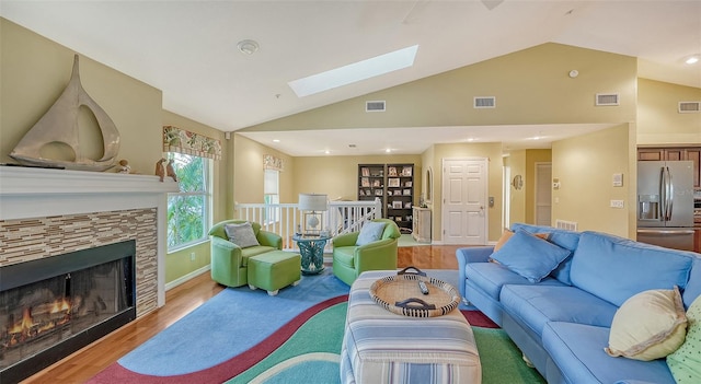 living room featuring a fireplace, light wood-type flooring, and vaulted ceiling with skylight