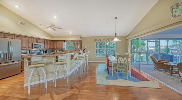 kitchen with a kitchen breakfast bar, hanging light fixtures, light wood-type flooring, backsplash, and appliances with stainless steel finishes