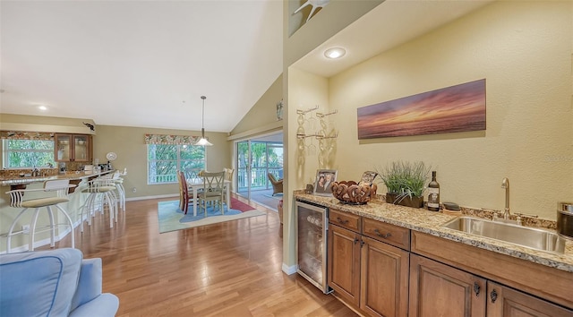 interior space featuring wine cooler, light stone counters, sink, pendant lighting, and light wood-type flooring